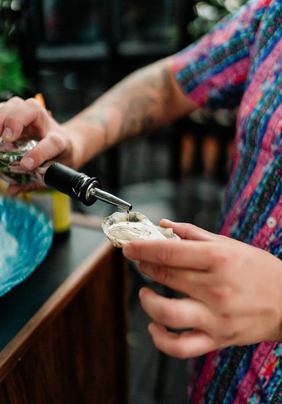 A hand pouring sauce onto a fresh oyster on the half shell at Borracho's